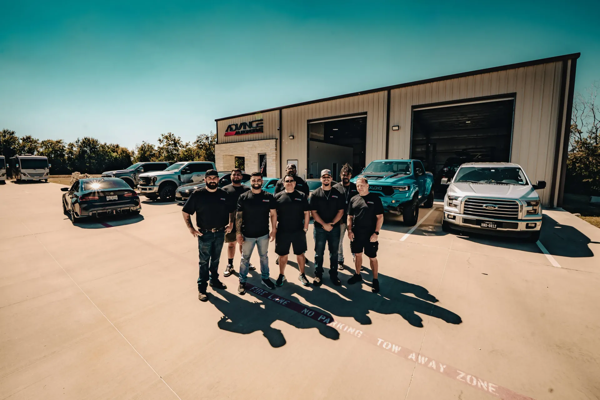 Group of men standing in front of a shop with several vehicles parked outside. | Advance Automotive