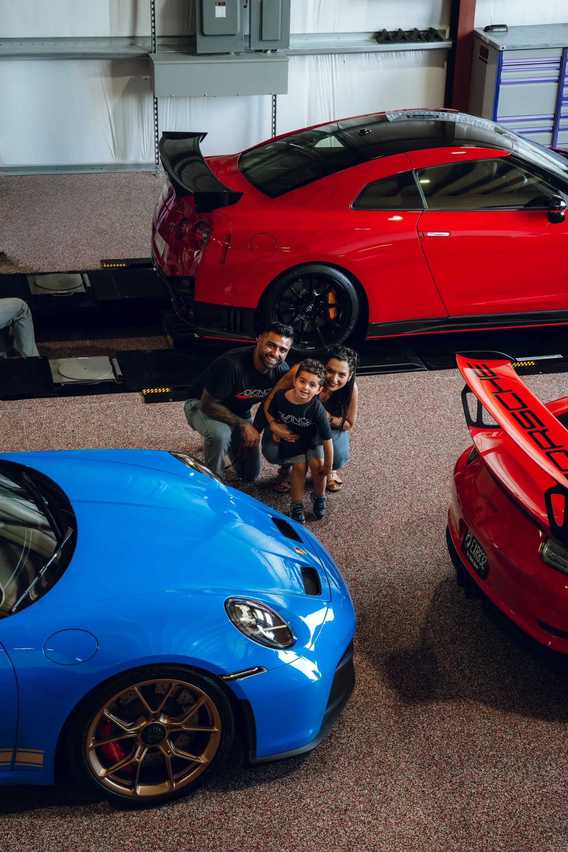 Family poses with sports cars, including a red Nissan GT-R and blue Porsche. | Advance Automotive