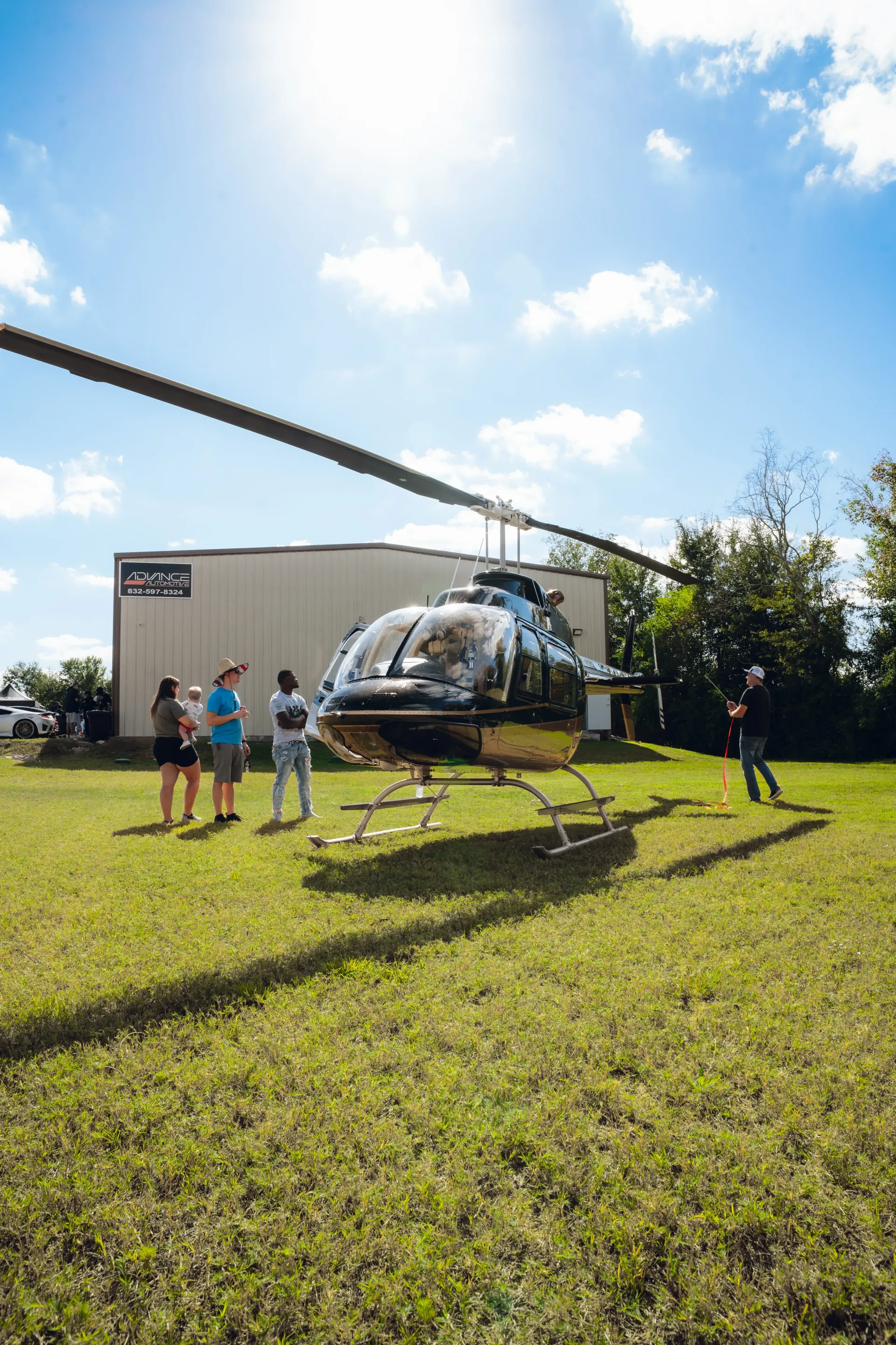 Helicopter on grass with people watching near a white building on a sunny day. | Advance Automotive