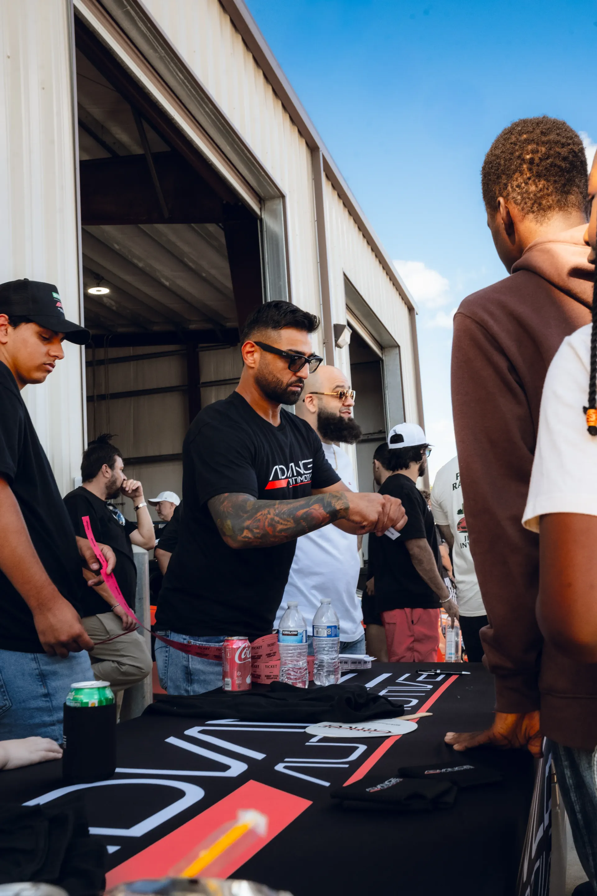 Man at table with merchandise, interacting with customers. Outdoor event with others nearby. | Advance Automotive