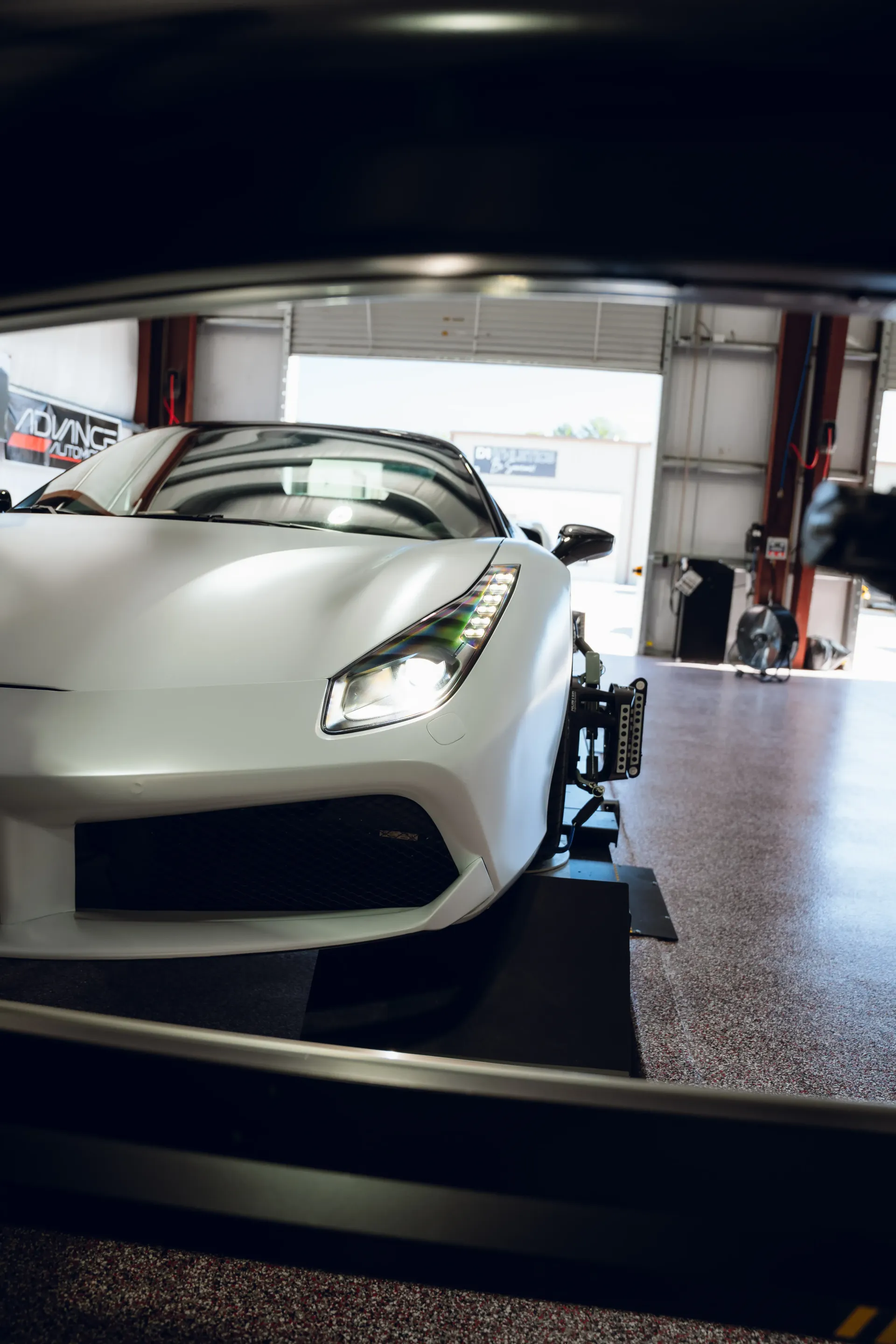 White sports car inside a garage, viewed through an opening. Headlights are on. | Advance Automotive