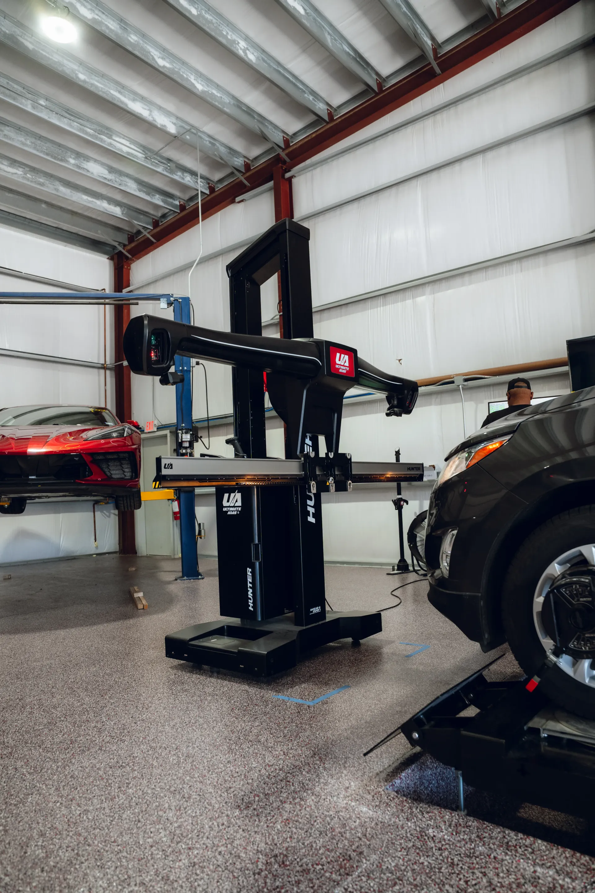Alignment machine in a garage, next to a car on a lift; a red sports car visible in the background. | Advance Automotive