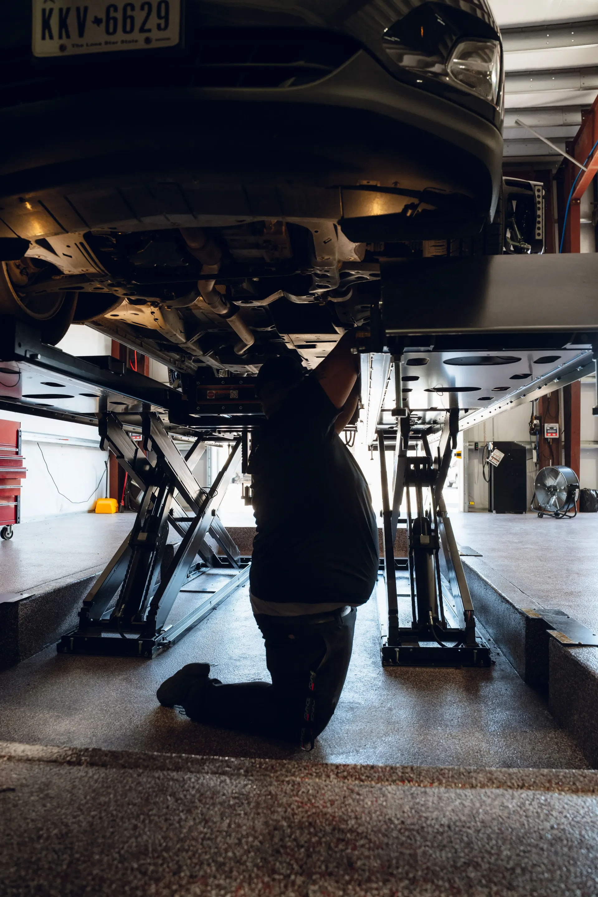 Mechanic working under a car lifted on a hydraulic rack in a garage. | Advance Automotive