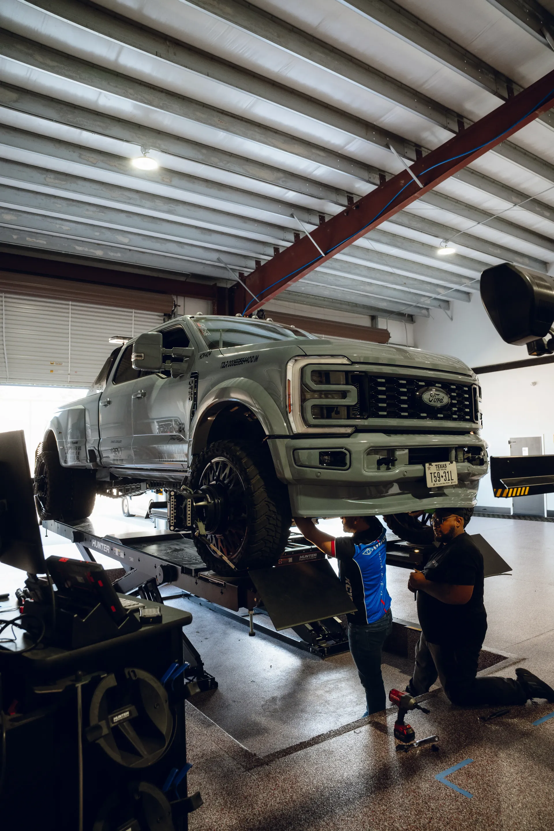 Gray truck on a lift in a garage; two mechanics working on it. | Advance Automotive