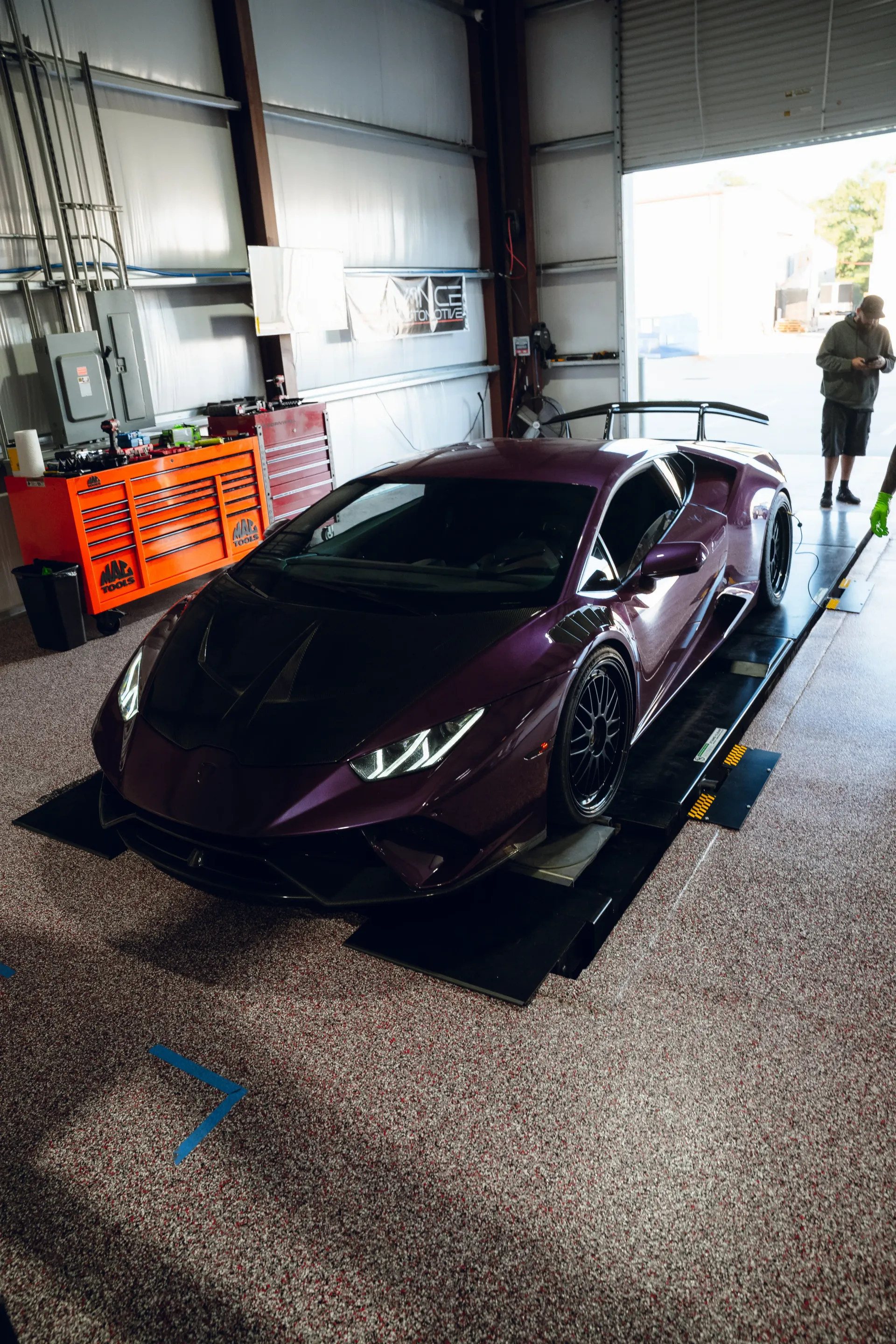 Purple Lamborghini on a lift in a garage with a person standing by the open door. | Advance Automotive