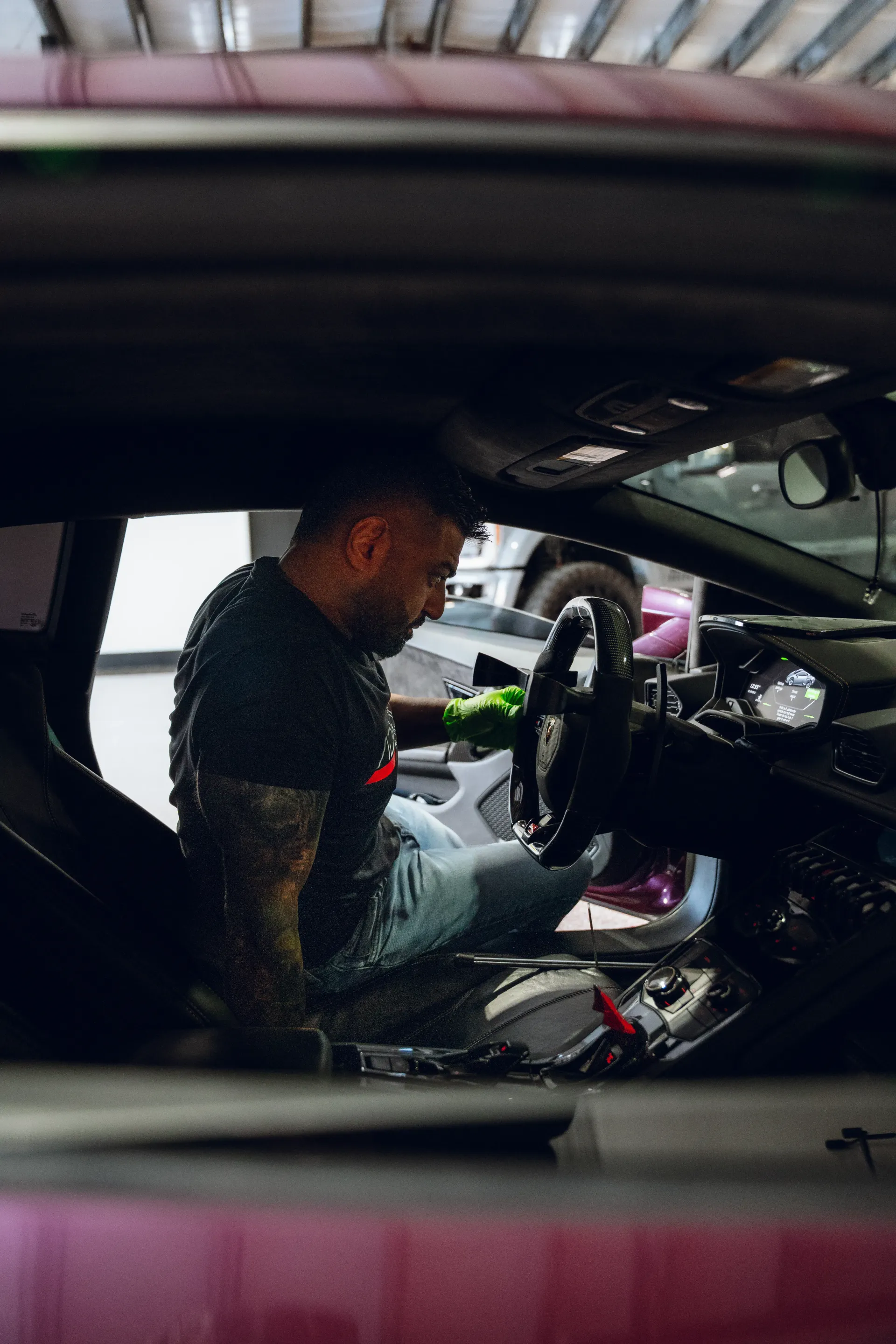 Man inside a car, working on dashboard. He has tattoos and wears a dark shirt and jeans, inside a garage. | Advance Automotive
