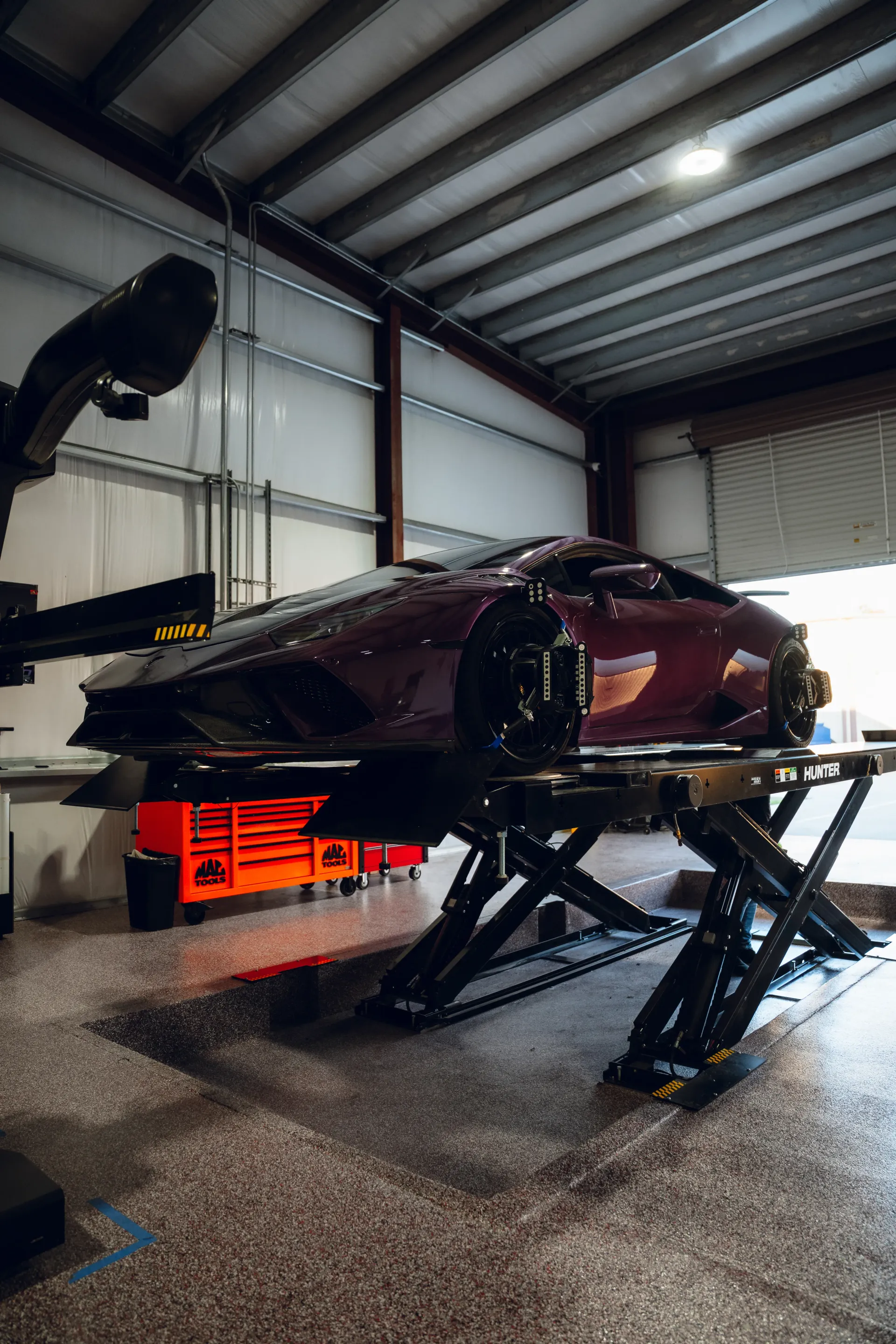 Burgundy sports car on a black lift in a garage with tools. | Advance Automotive