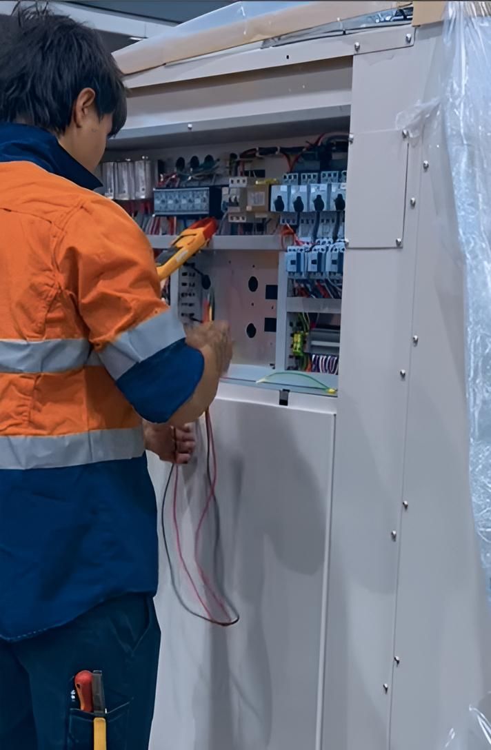 A Man in an Orange Shirt is Working on a Electrical Box — FVS Airconditioning & Electrical Pty Ltd in Doomadgee, QLD