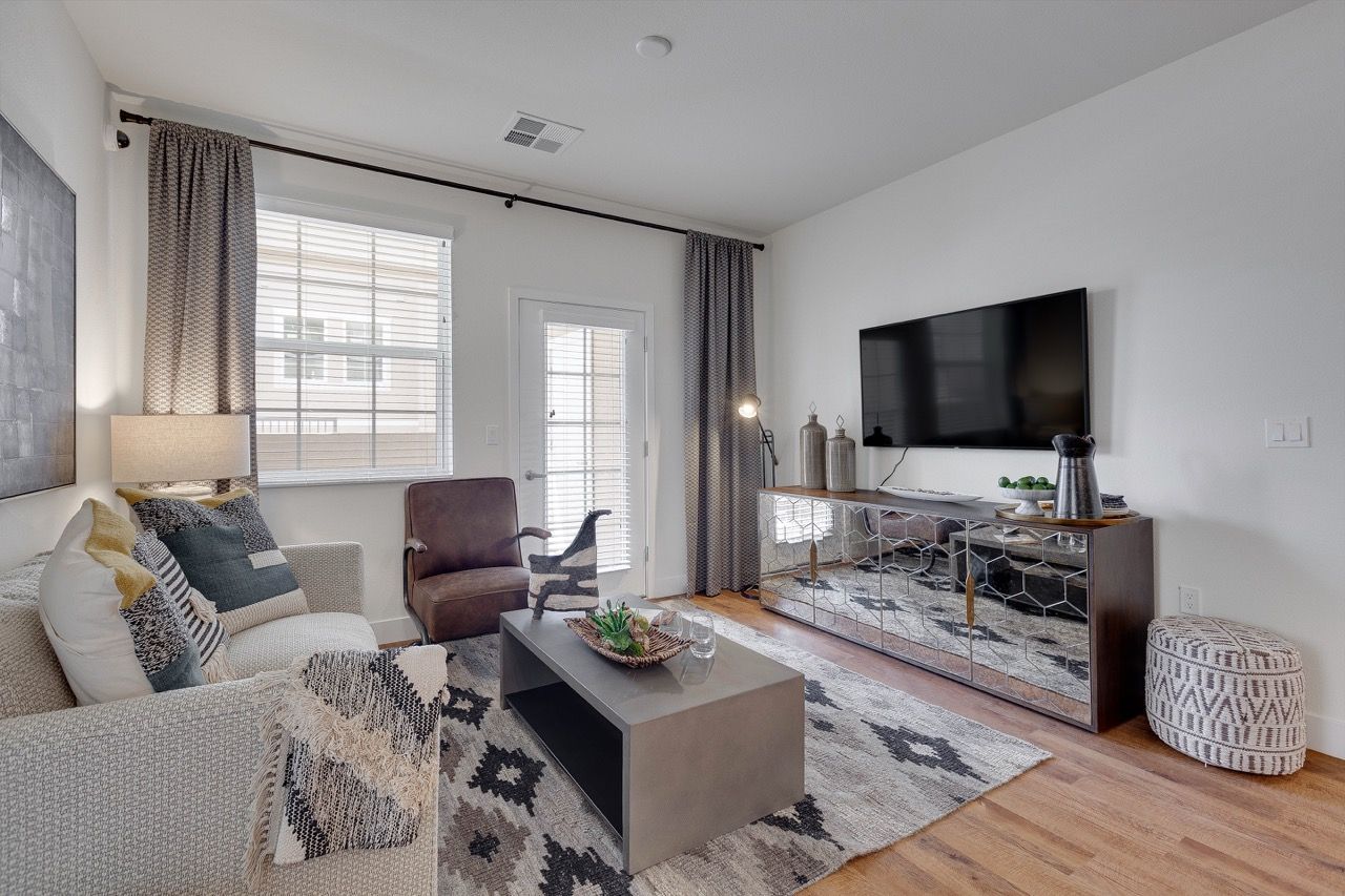 Bright living room with neutral sofa, armchair, coffee table, and wall-mounted TV.