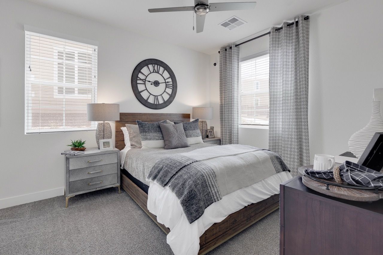 Bedroom in a modern apartment with a wooden bed, gray bedding, two nightstands, and large windows.