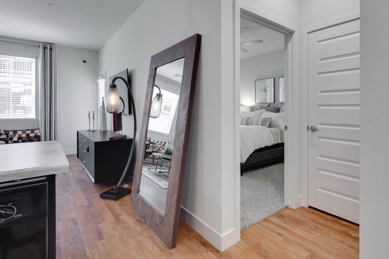 Interior view of a modern apartment with hardwood floors, a leaning mirror, and a doorway to a bedroom.
