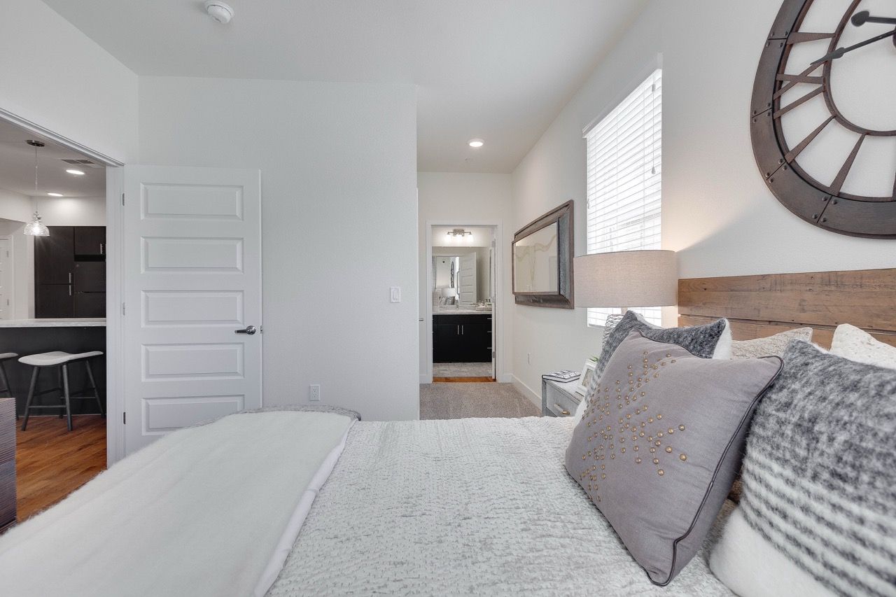 Bedroom in a modern apartment with a wooden headboard, decorative pillows, and a large wall clock.
