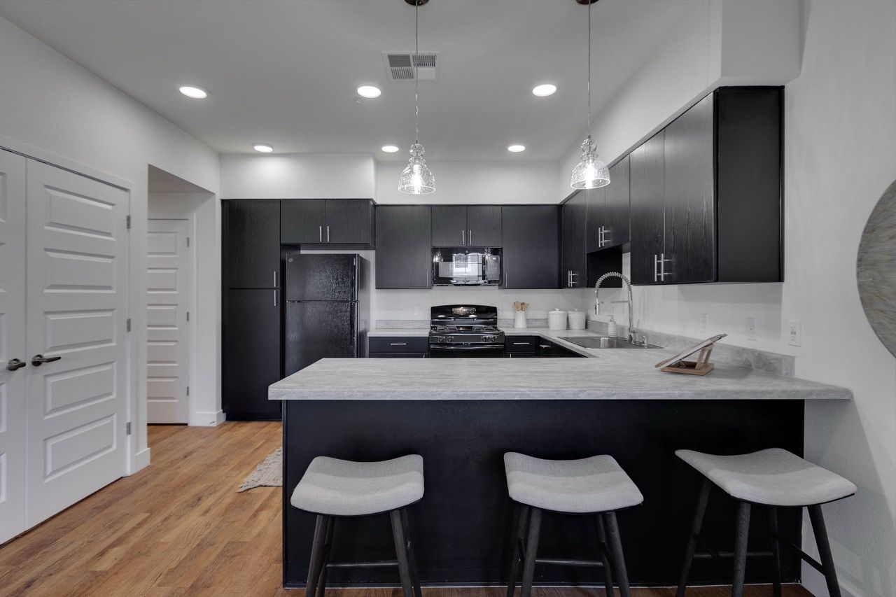Modern black kitchen with island, pendant lights, and three bar stools.