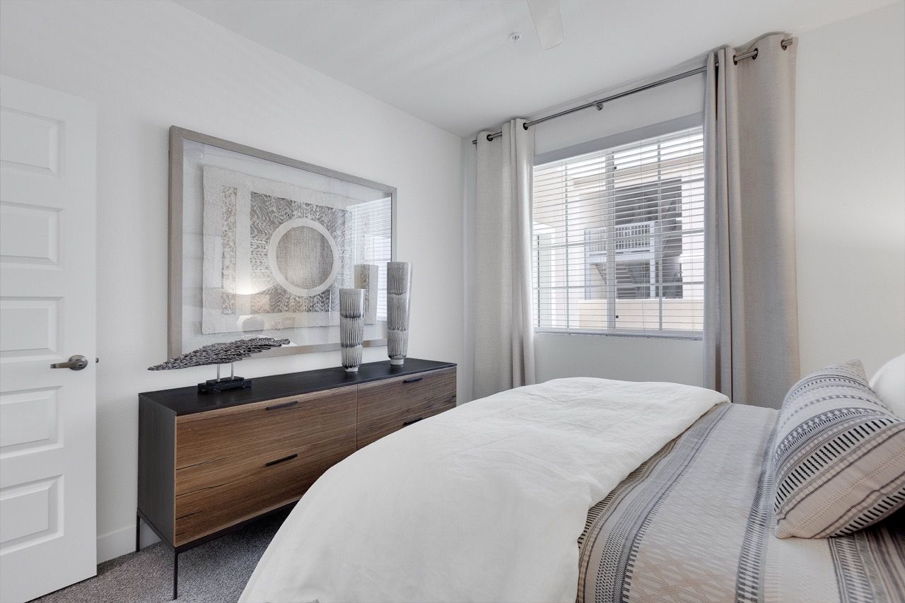 Bedroom with a wooden dresser, wall art, and a window with blinds.