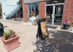 Storefront with sidewalk display, sandwich board sign, potted flowers, and brick building exterior