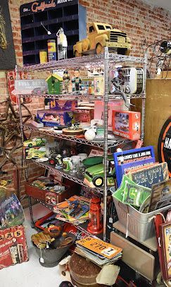 Cluttered shop display with shelves of colorful toys, tools, and assorted small goods against a brick wall.