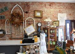 Vintage shop interior with brick wall, framed decor, and assorted antiques, including a white dress mannequin