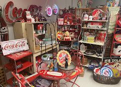 Colorful vintage Coca-Cola collectibles displayed on shelves and tables in a cluttered room
