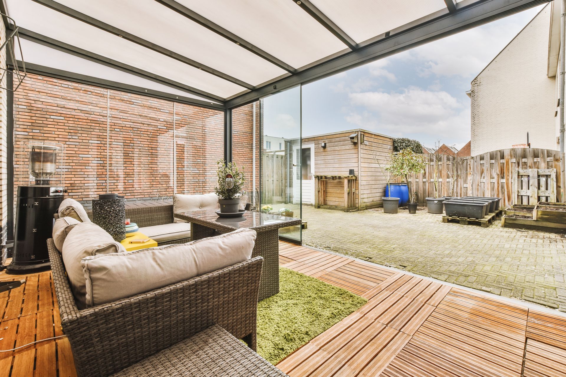 Patio with wicker furniture, glass walls, and wood flooring overlooking a backyard.