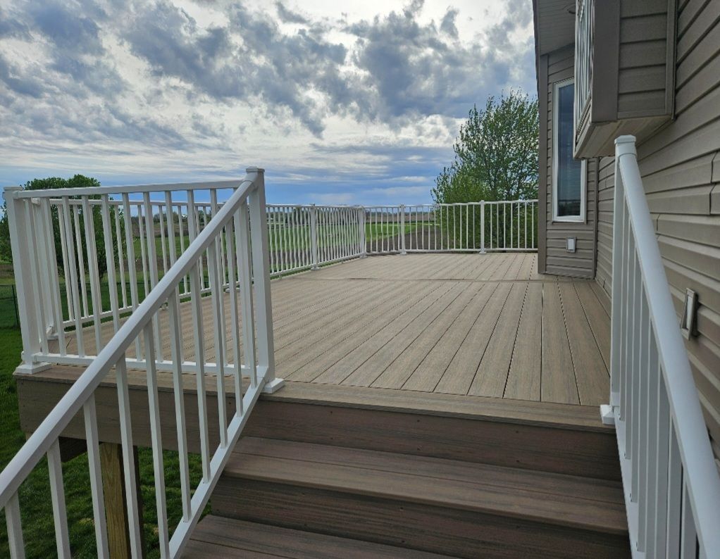 A wooden deck with white railings, overlooking a cloudy sky and green landscape.