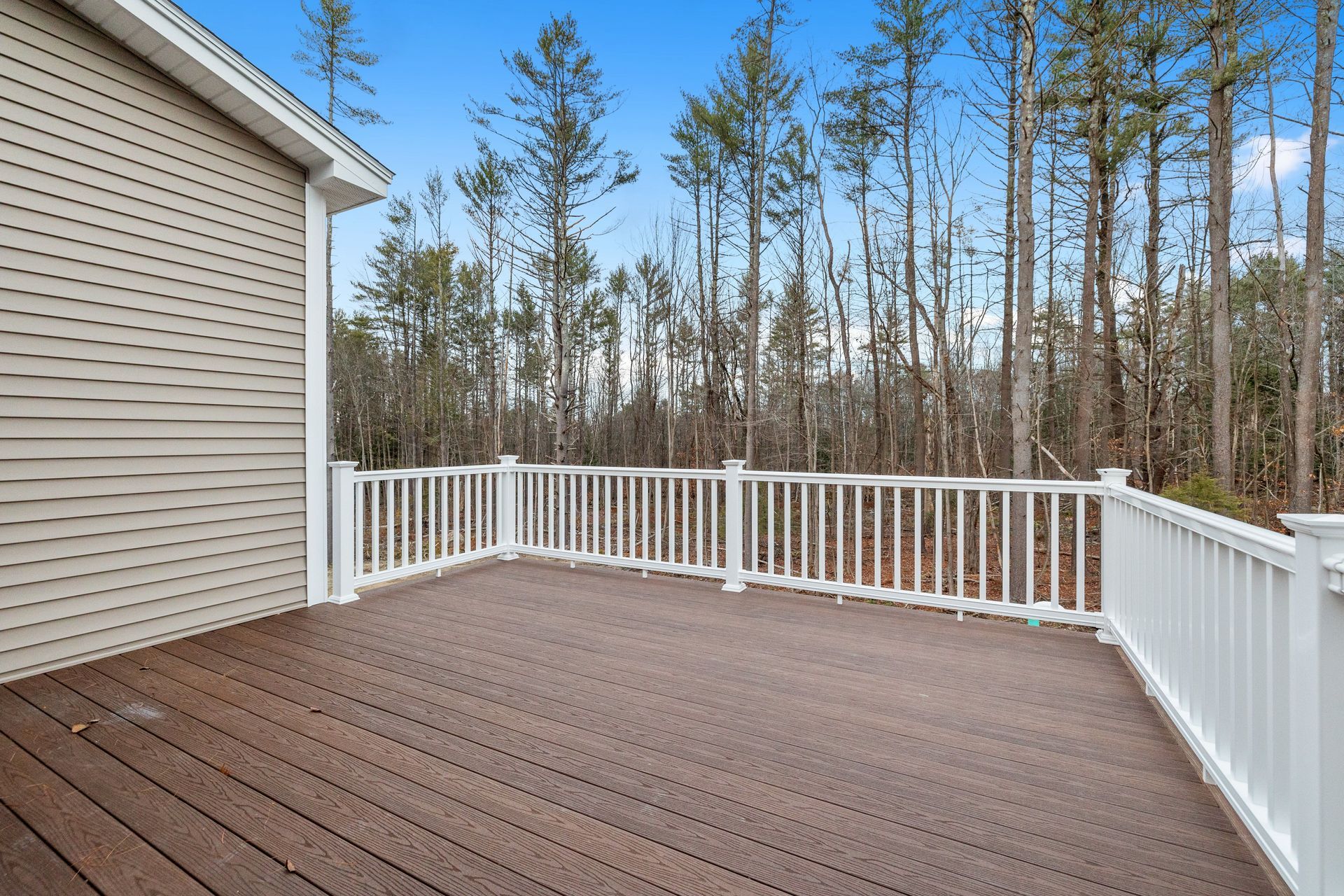 Deck with white railing, brown composite floor, and a wooded backdrop.