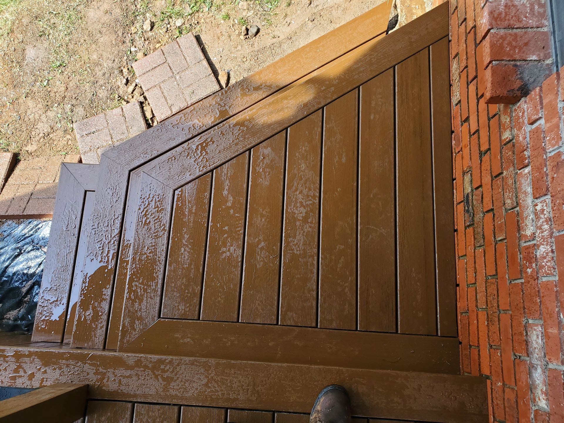 A person is standing on a wooden deck next to a brick wall.