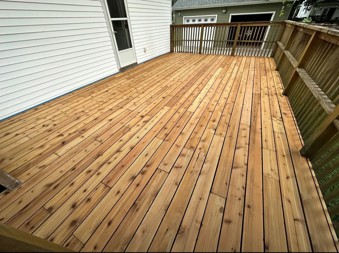 Wooden deck extending from a white-sided house, with railings and a view of a garage.