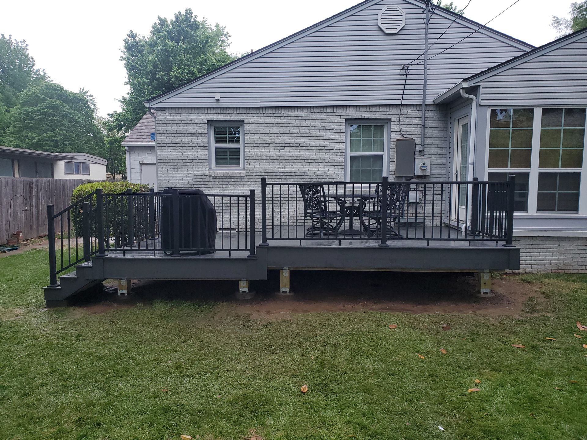 Back deck with black railing and patio furniture attached to a gray house