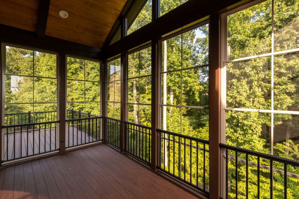 Wooden screened porch with black railings and large windows overlooking green trees
