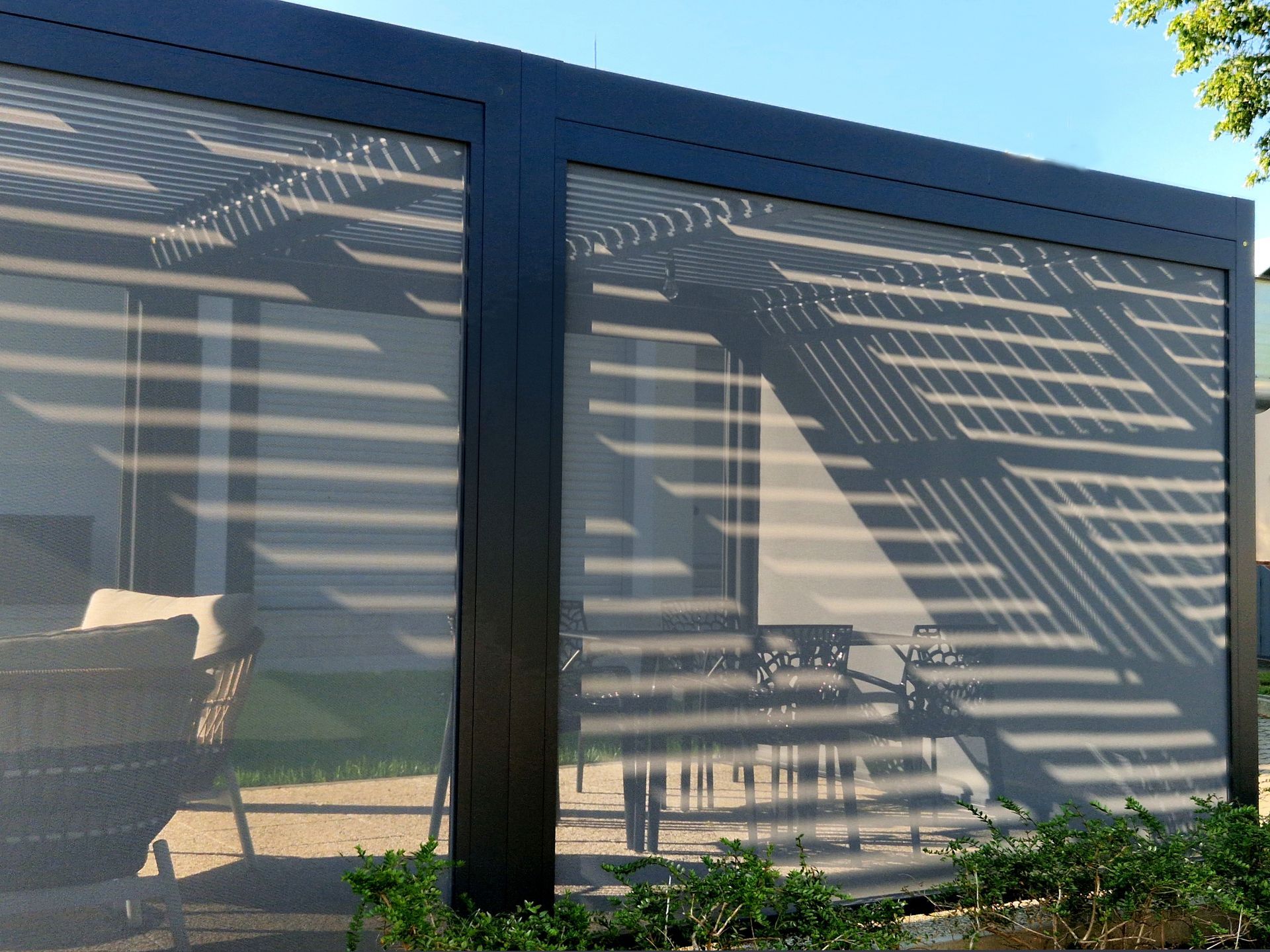 Black-framed screened patio with striped sunlight and outdoor chairs inside