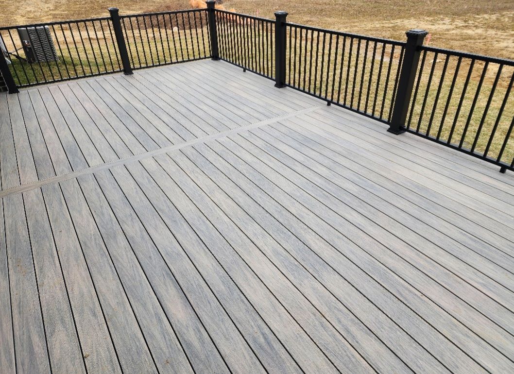 A wooden deck with a black railing and a grassy field in the background.