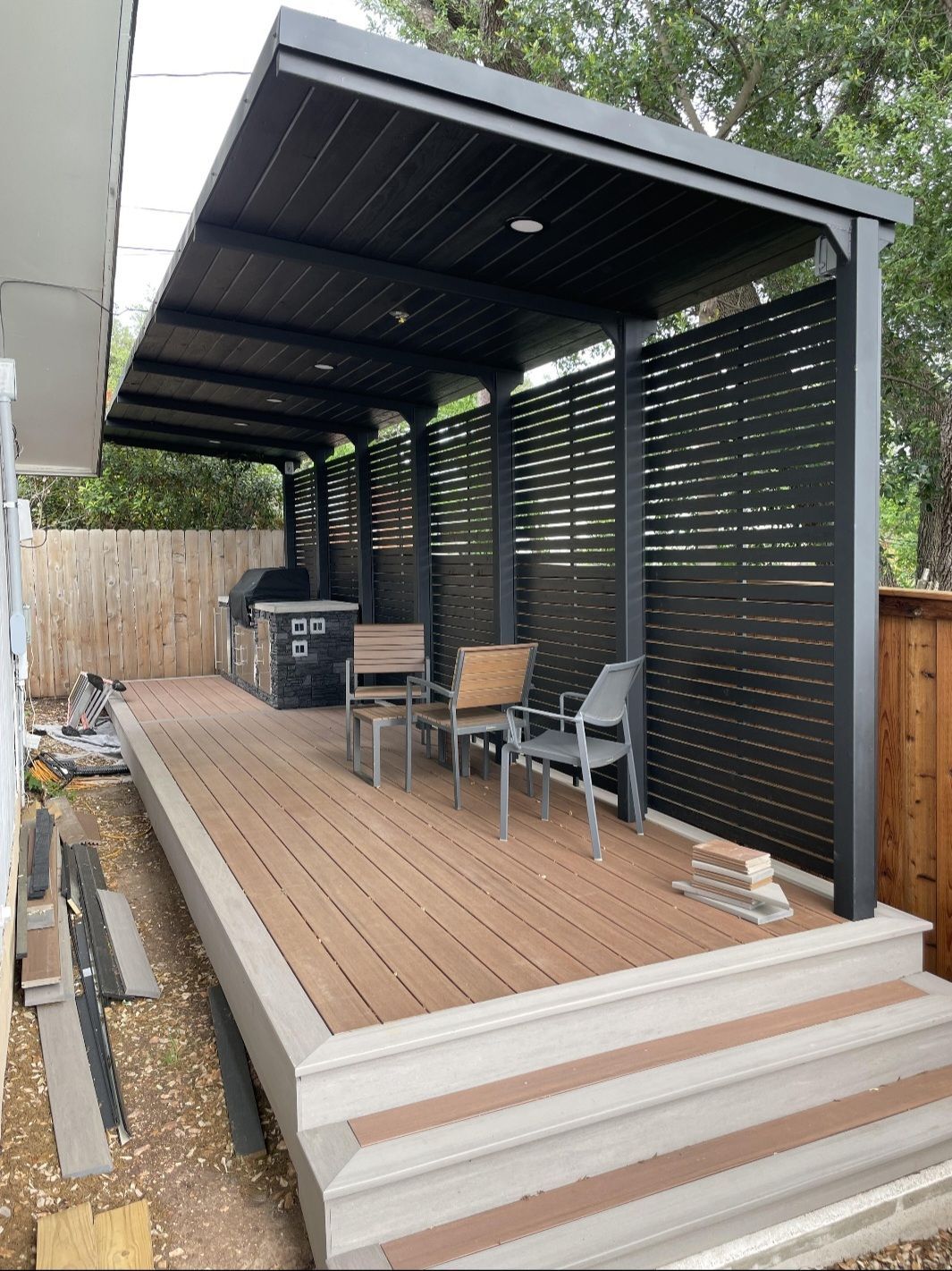 A wooden deck with a covered area and chairs underneath it.