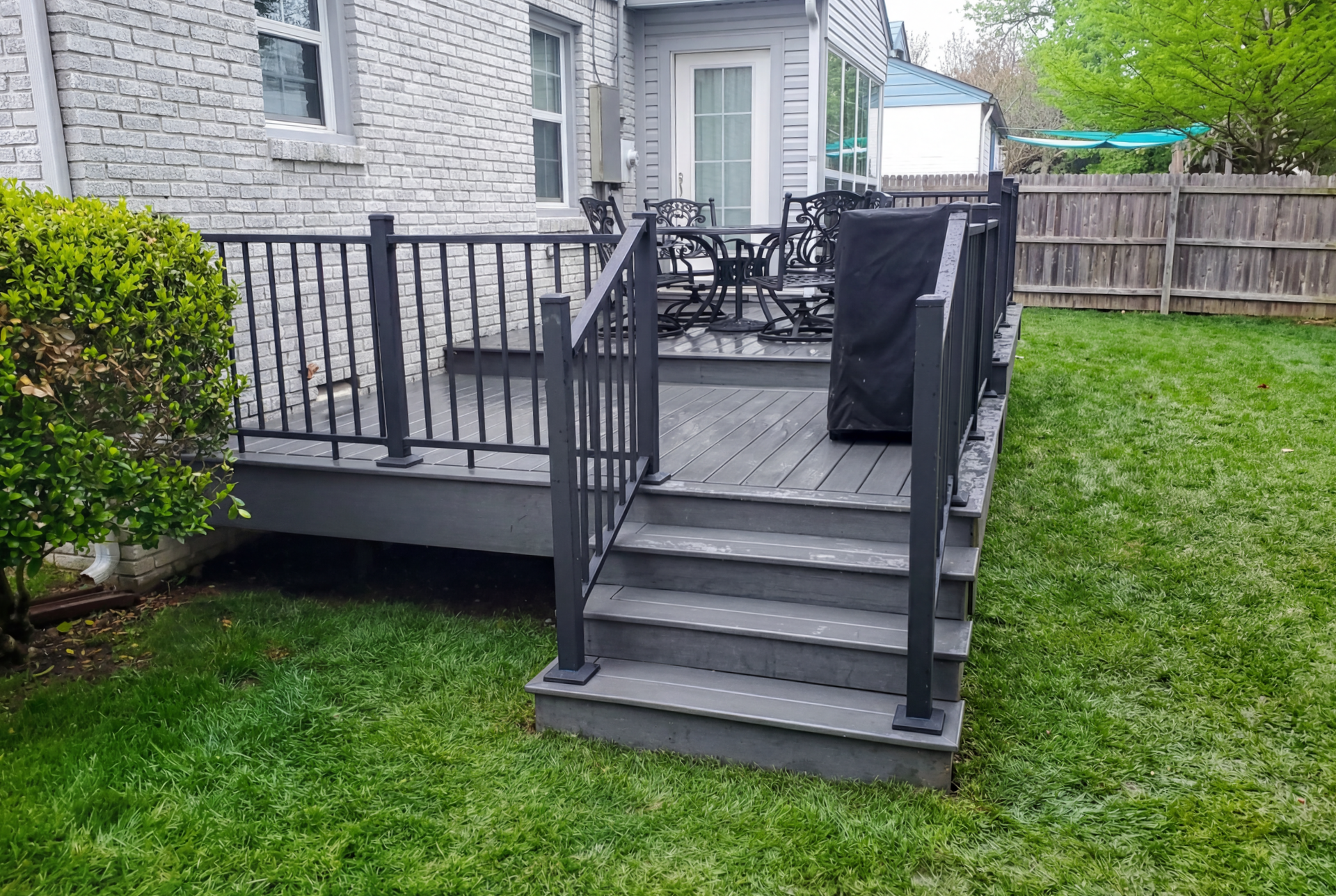 A deck with stairs and a grill in the backyard of a house.