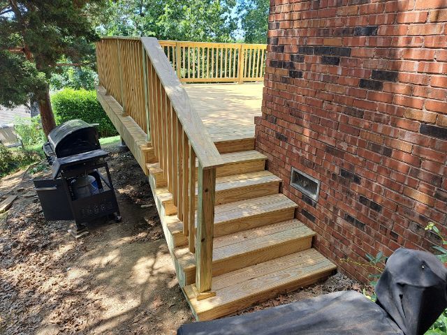 A wooden deck with stairs leading up to it next to a brick wall.