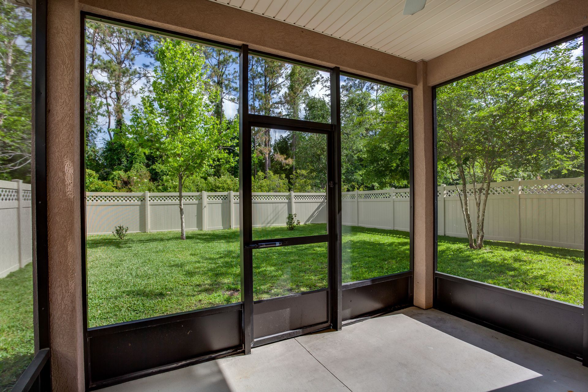 A screened in porch with a fence and trees in the background.