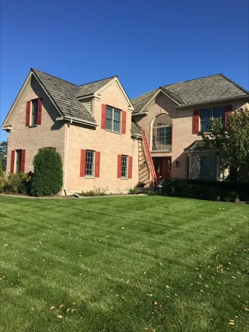 A large brick house with red shutters and a lush green lawn in front of it.