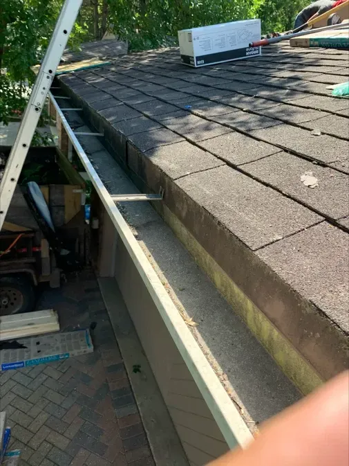 A person is holding a gutter on top of a roof.