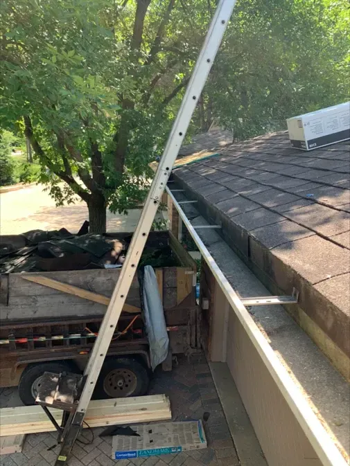 A ladder is hanging over a gutter on a roof.