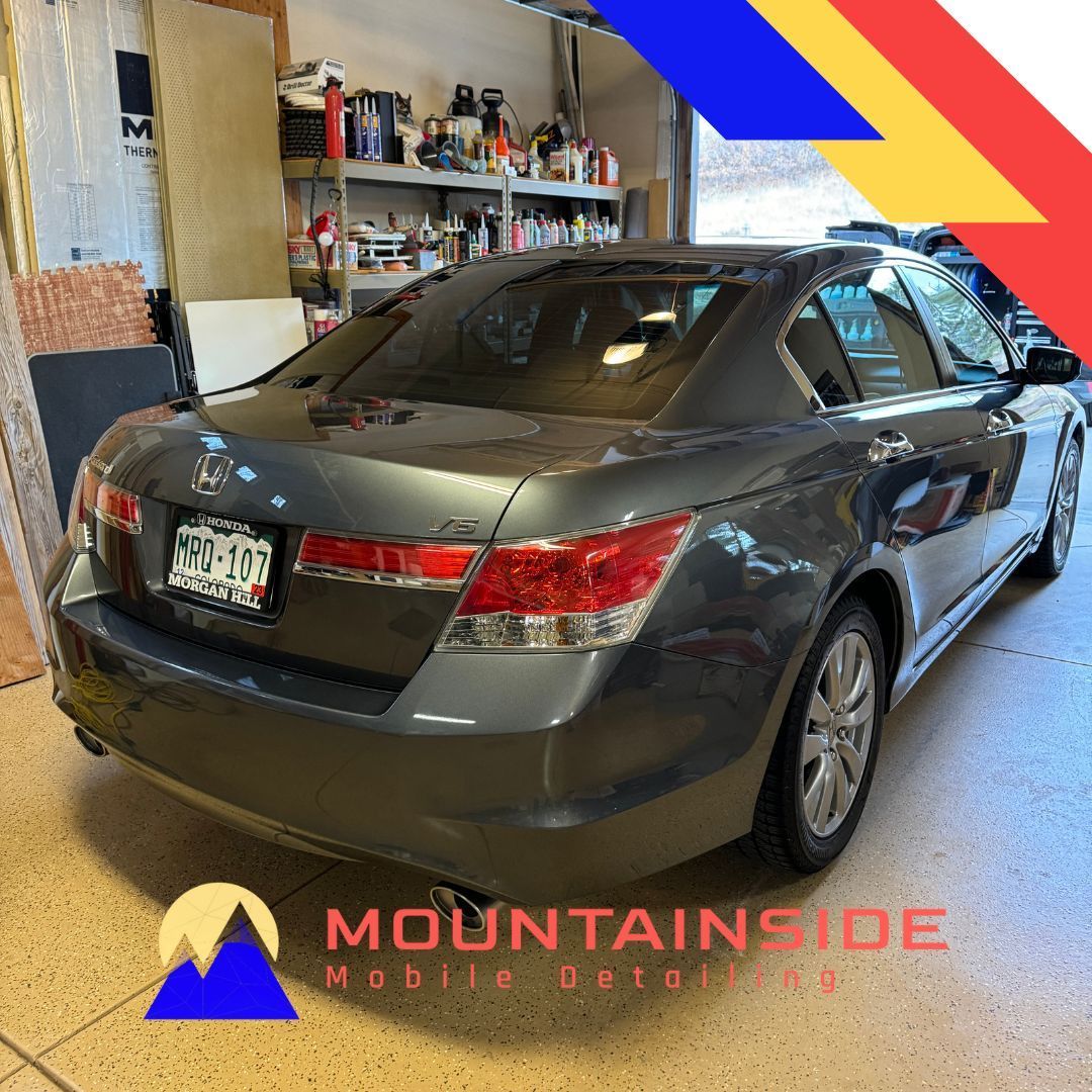 A gray car is parked in a garage with a mountain inside logo