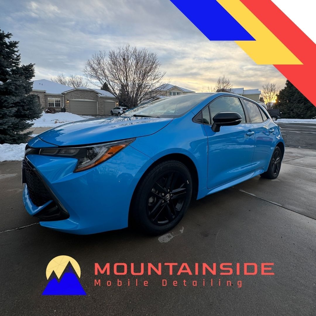 A blue car is parked in front of a mountainside mobile detailing logo