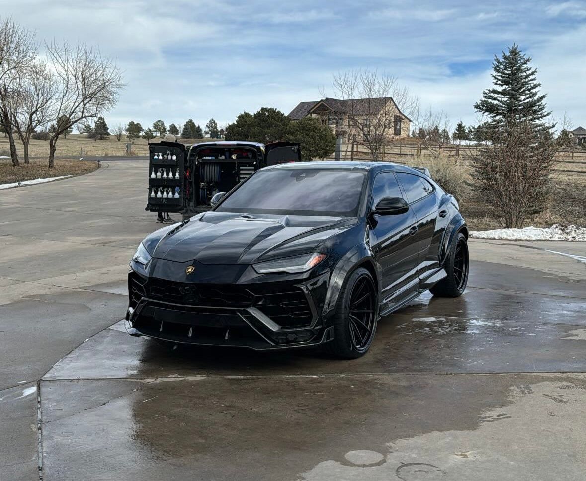 A black lamborghini urus is parked in a parking lot.
