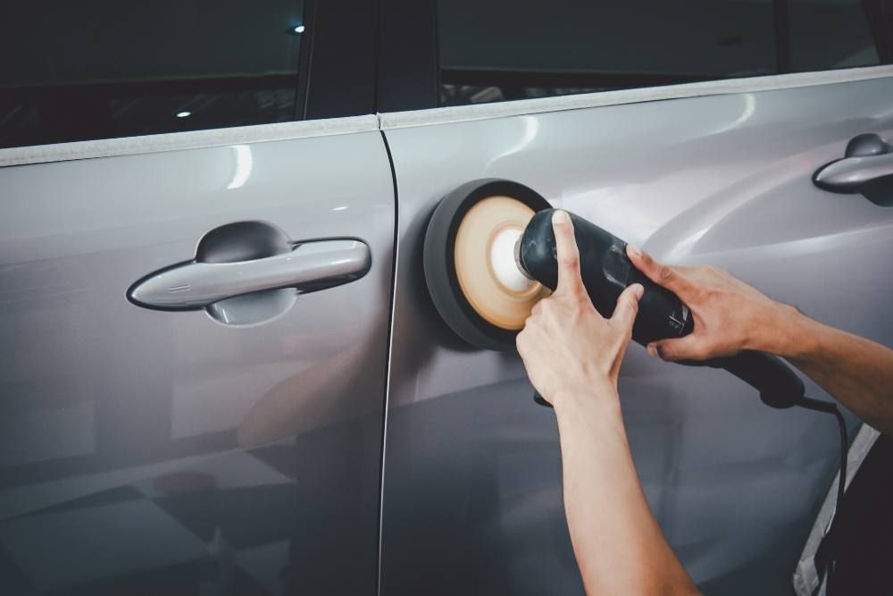 A person is polishing a car door with a polisher.