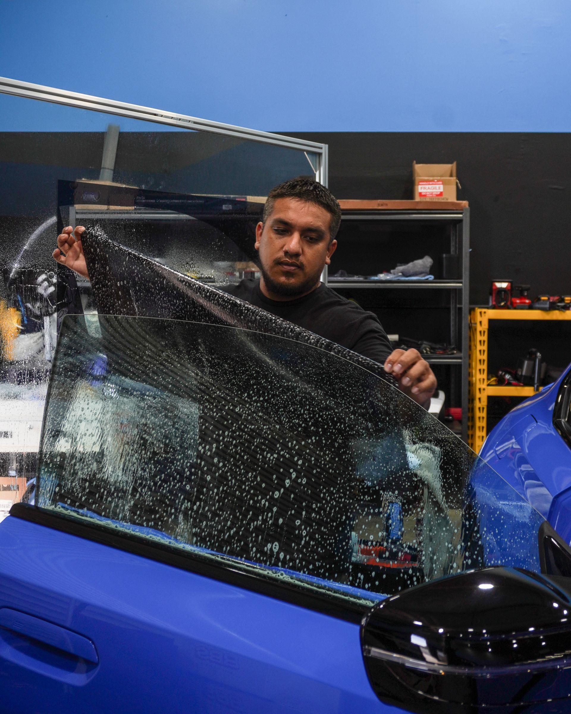 Man tinting a car window with a large sheet of film inside a garage