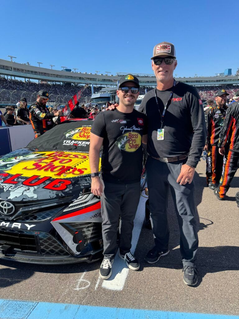 Two men are standing next to each other in front of a race car.