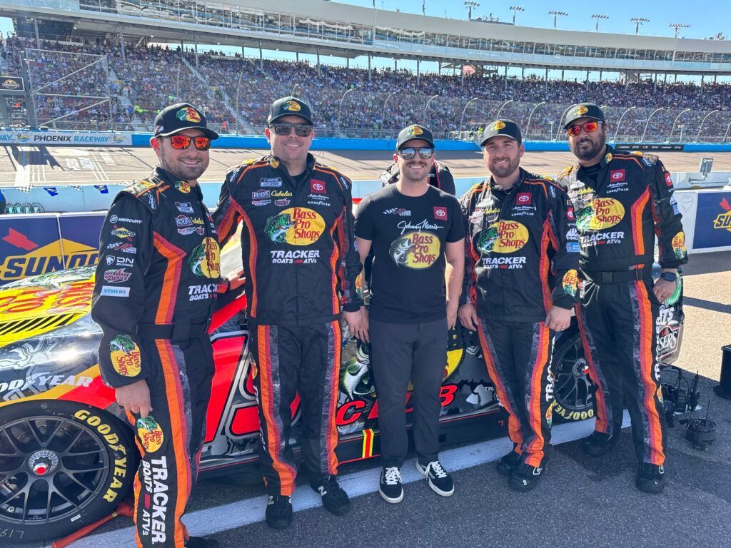 A group of men are standing next to a race car on a race track.