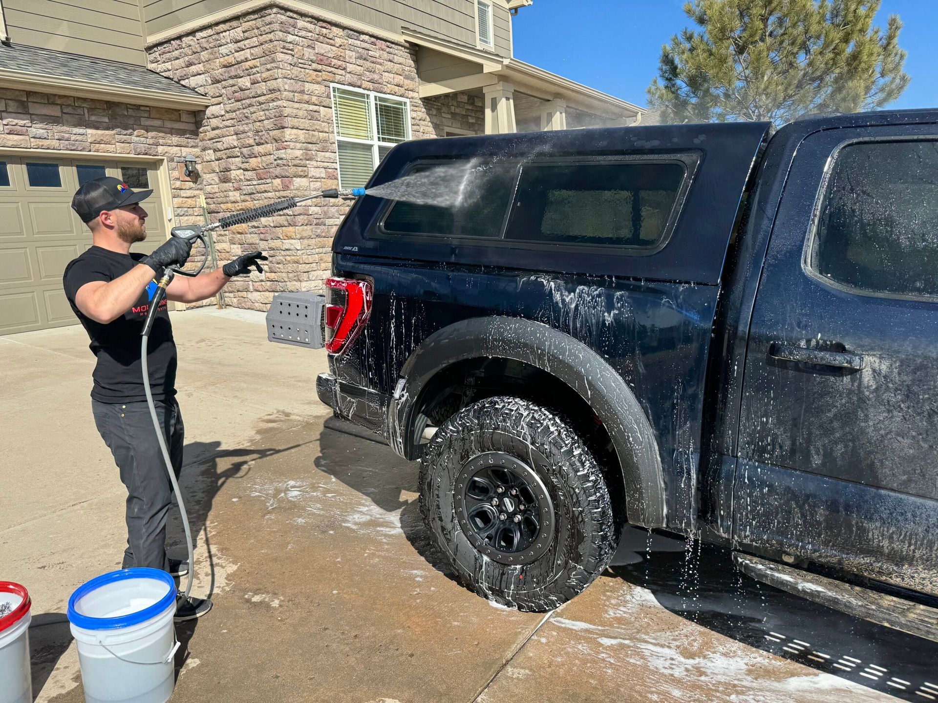 A man is washing a black truck with a high pressure washer.