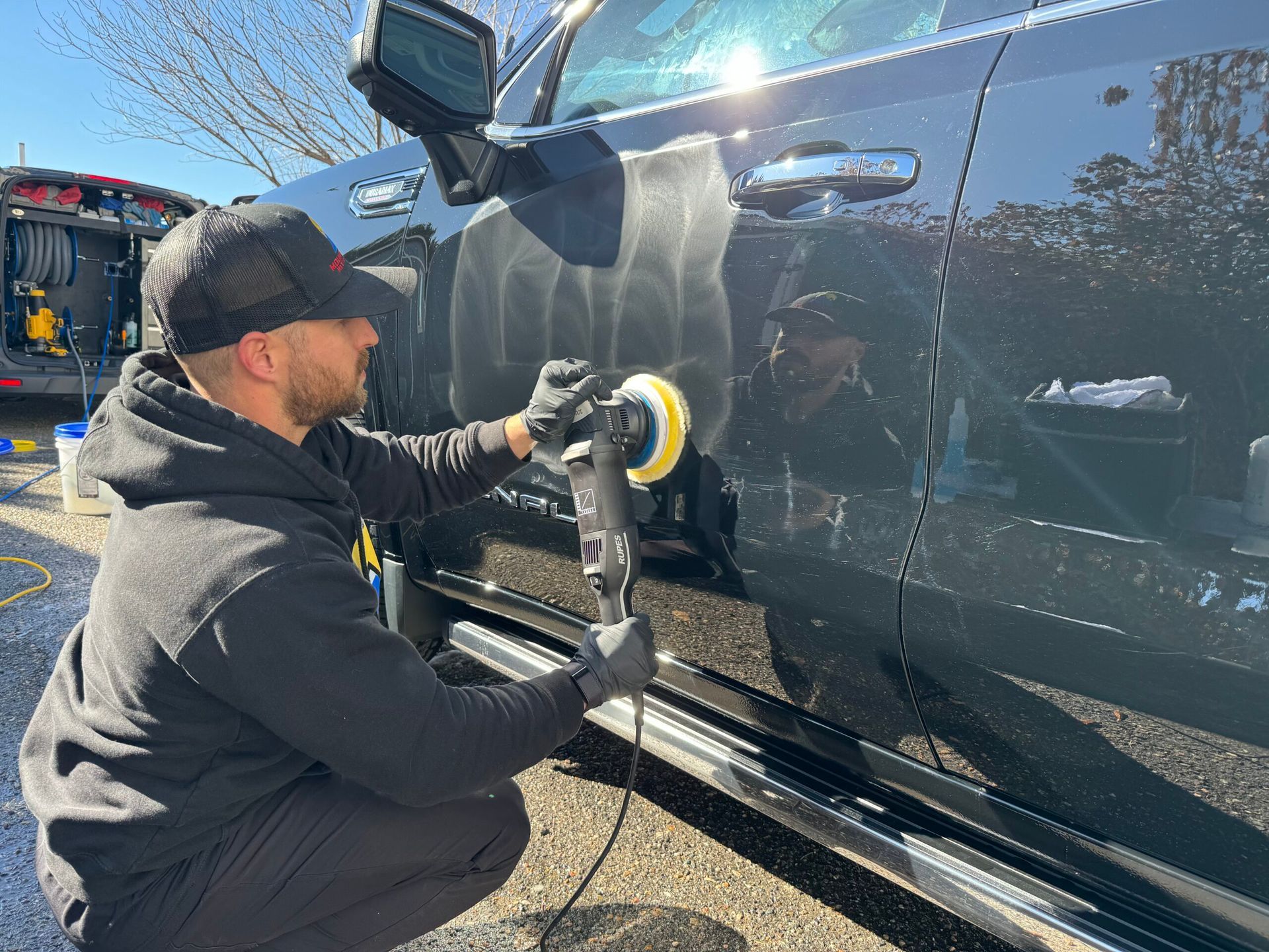 A man is polishing a black truck with a machine.