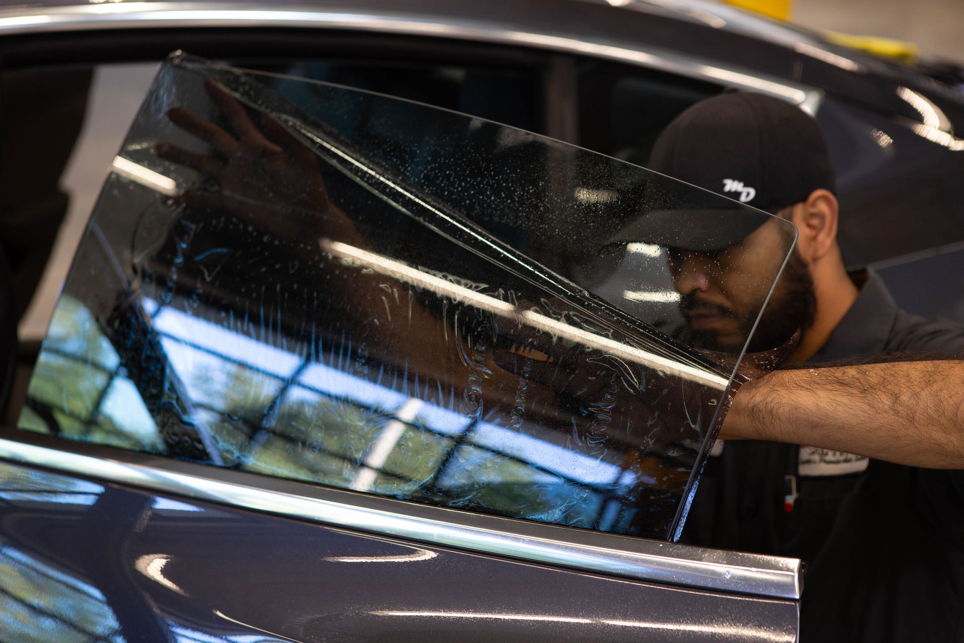 Man installing a tinted car window film in a workshop