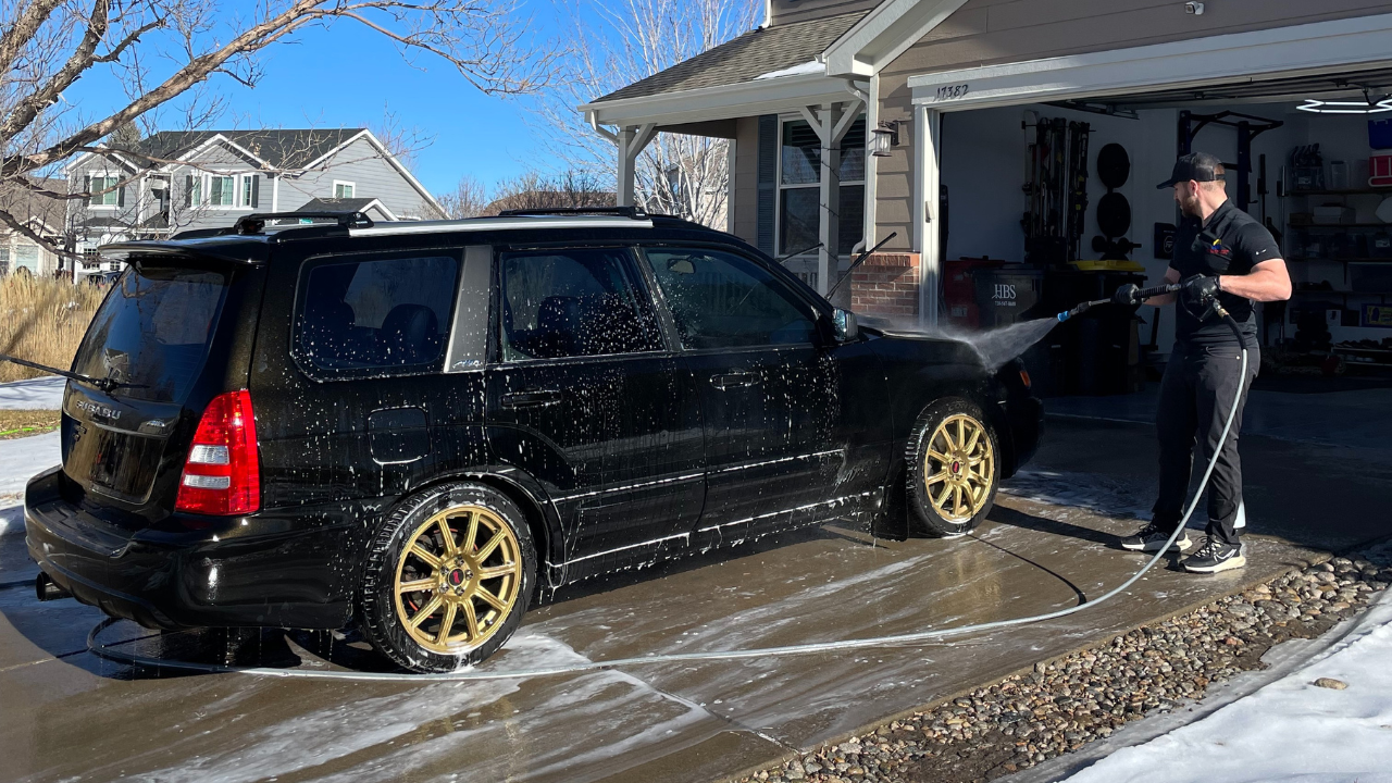 A man is washing a black suv with a high pressure washer.