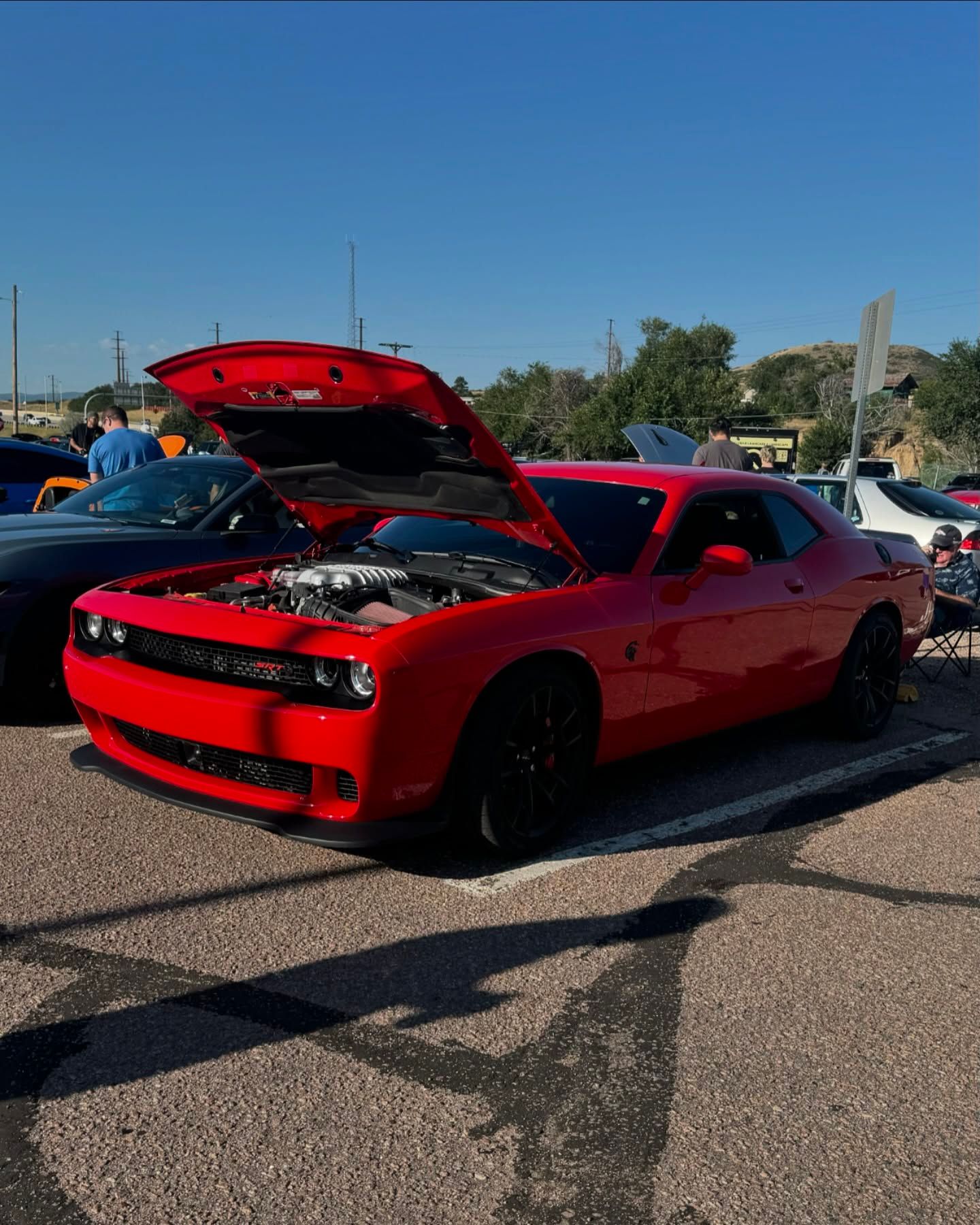 A red dodge challenger with the hood up is parked in a parking lot